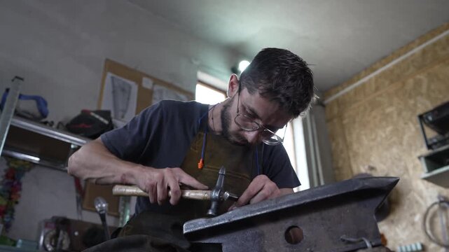 Blacksmith hammering a metal punch on an anvil in a workshop