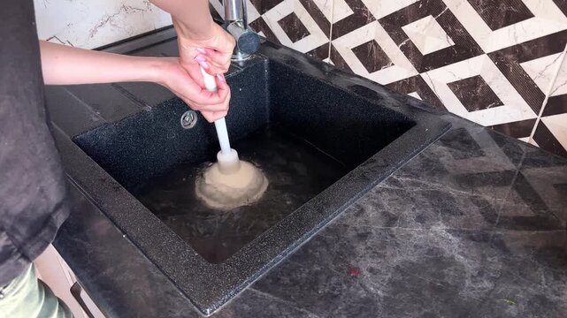Person's hands using a white rubber plunger to clear a slow kitchen sink drain