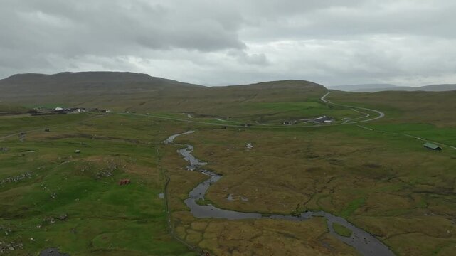 A push in drone shot shows farms and winding river Sand&aacute; amidst the lush, hilly landscape on the Faroe Islands.