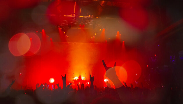 Crowd of people with heavy metal devil horn sign mano cornuta hands up at live rock music concert show in spotlight and band group real photo, no ai