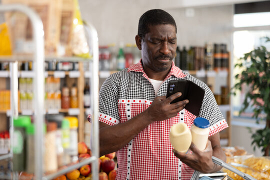 African male client scans QR code on mayonnaise package, reads product information in mobile application. Man points smartphone camera at code and reads information on label.