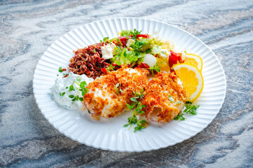 Fototapeta premium Traditional Mediterranean recipe - breaded buttered crispy fried calamari with greek salad, brown rice and tzatziki served on a design plate