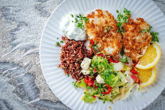 Traditional Mediterranean recipe - breaded buttered crispy fried calamari with greek salad, brown rice and tzatziki served as top view on a design plate