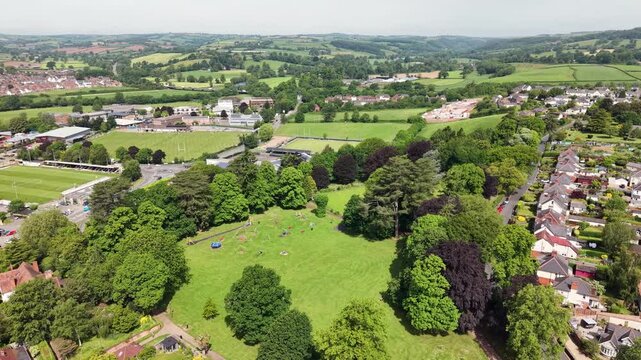 Cinematic aerial drone footage showcasing the historic market town of Tiverton in Devon, England. The flight captures the town, residential neighborhoods, architecture, surrounding countryside