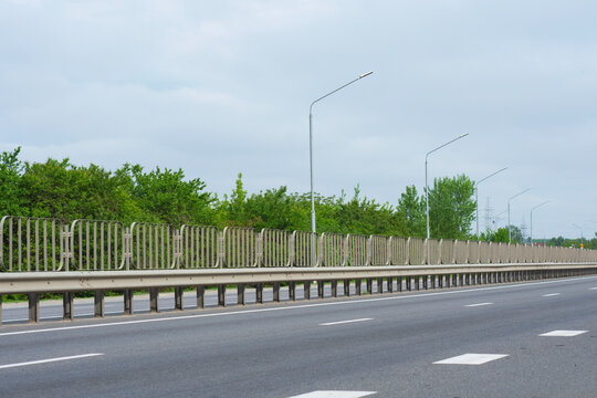Empty asphalt highway road with metal guardrail barrier and street lights. Transportation infrastructure development, international logistics route or corporate commercial logistics banner concept.