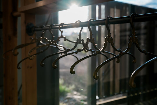 Vintage Ornate Metal Coat Hangers Backlit by Warm Sunlight Creating Elegant Boutique Wardrobe Storage Concept with Decorative Ironwork and Atmospheric Interior Details