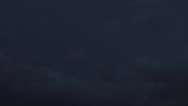 Distant thunderclouds glowing with lightning in dark night sky