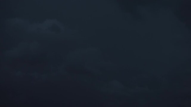Nighttime lightning flashes across rolling black storm clouds