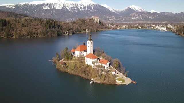 Aerial view of Lake Bled and the Pilgrimage Church of the Assumption of Maria on the island, with snow-capped mountains in the background in Bled, Radovljica, Slovenia.