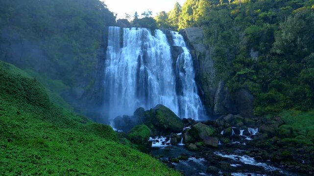 Side View of Marokopa Falls Cascading Behind Green Forest Hill Foreground