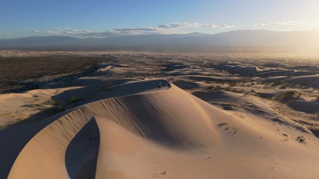 Aerial view of Dunas de Taton with people walking along the ridge of the sand dunes during golden hour in Tinogasta Department, Catamarca Province, Argentina.