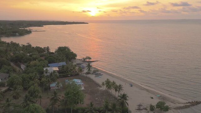 Aerial view of the sandy beach and lush palm trees along the coastline of Covenas during a golden sunset in Covenas, Sucre, Colombia.