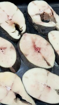 White fish slices on tray supermarket counter, fresh oily texture, pale flesh with pink centers, neatly arranged rows in black