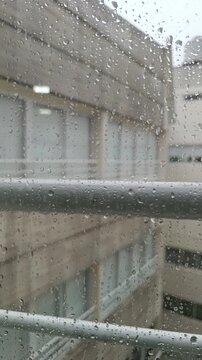 Rainy day through a window glass against a blurred buildings  background.