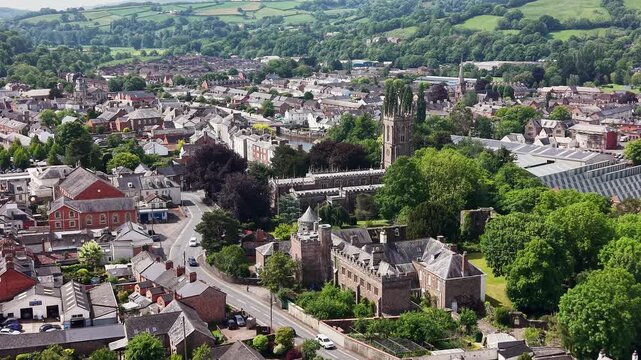 Cinematic aerial drone footage showcasing the historic market town of Tiverton in Devon, England. The flight captures the town, residential neighborhoods, architecture, surrounding countryside