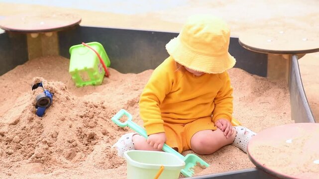  Toddler boy digging and pouring sand into bucket at playground