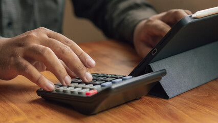 Fototapeta premium Close Up of Hands Using A Calculator and Tablet on Wooden Desk