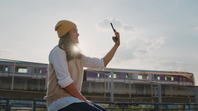The way forward Agentic AI living future social media. Young adult gen z woman asia people relax smile happy asian content creator using camera mobile phone in smart city urban life metro sky train.