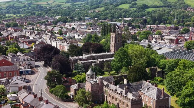 Cinematic aerial drone footage showcasing the historic market town of Tiverton in Devon, England. The flight captures the town, residential neighborhoods, architecture, surrounding countryside