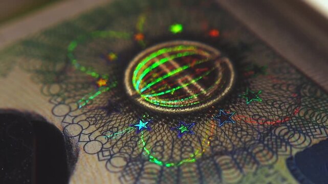 A close-up of the illuminated holographic emblem of the EU Schengen visa. The iridescent multicolor security hologram of the Schengen visa of the European Union countries. 4k slow motion video