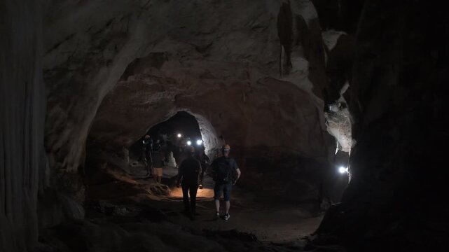 visitors exploring the vast chambers of Khao Wang Thong Cave in southern Thailand, illuminated by headlamps that reveal dramatic limestone formations and the cave's mysterious underground atmosphere.
