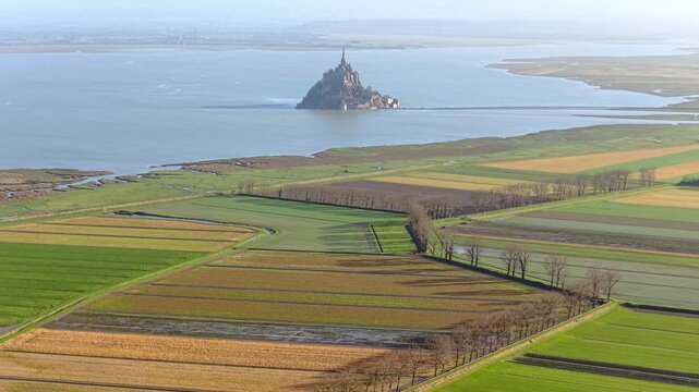 Aerial view of the historic Mont Saint-Michel abbey rising above the surrounding tidal flats and agricultural fields in Mont Saint-Michel, Normandy, France.