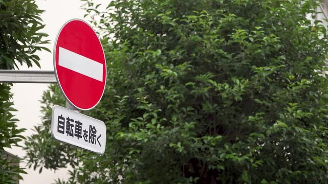 Left-positioned no entry road sign with bicycle exception in light rain on a Tokyo morning