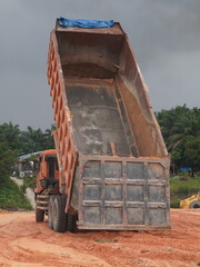 A large orange industrial dump truck with its heavy metal cargo bed raised high at a busy construction site area © emenbi