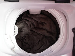 A soft dark brown fleece blanket sits inside the circular white drum of an open top loading washing machine appliance © emenbi