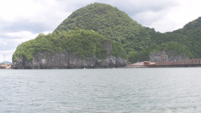 approaching the scenic khanom coastline in southern thailand, featuring a lush limestone hill, calm gulf waters, and dramatic tropical shoreline under a cloudy sky