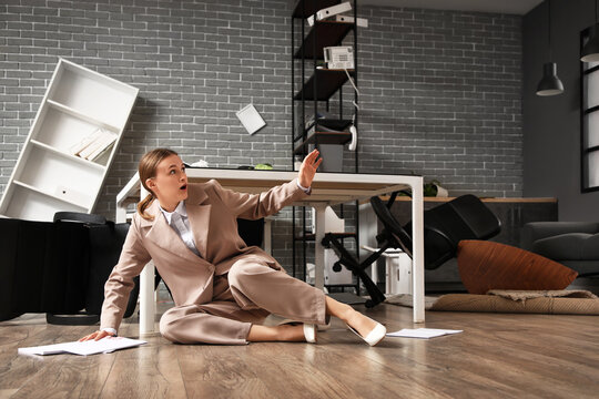 Scared businesswoman sitting near desk in office during earthquake