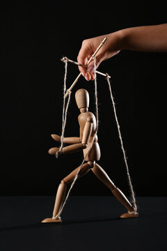 Hand of puppeteer manipulating marionette on black background