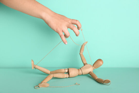 Hand of puppeteer manipulating marionette on turquoise background