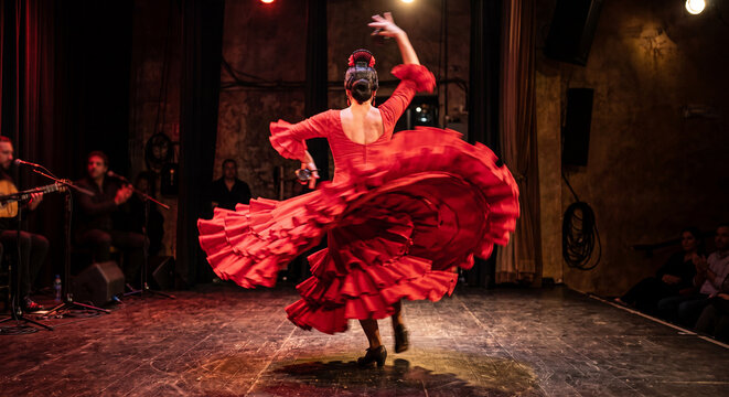Flamenco Dancer's Passionate Spin: A captivating flamenco dancer in a vibrant red dress performs a dramatic spin on stage, her voluminous skirt swirling with energy, accompanied by live musicians.