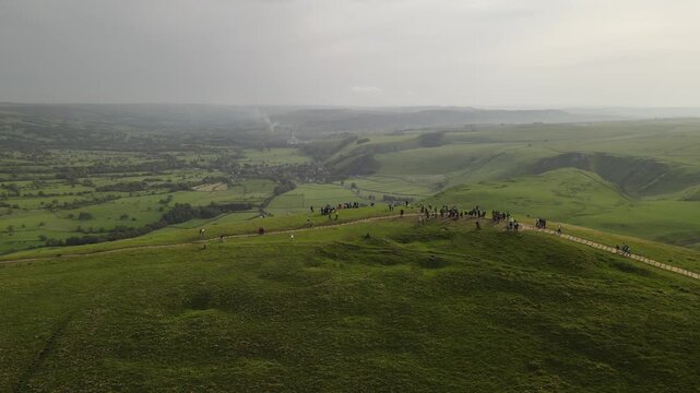 Aerial view of Mam Tor featuring a winding path along the grassy ridge with people walking and expansive green hills in the background in Castleton, England, United Kingdom.