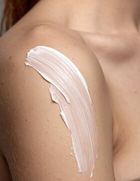 White cream smeared on a woman's shoulder, closeup of skincare application, cosmetic moisturizer, dermatological body lotion, beauty treatment, skincare.