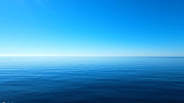 Slow pan across a tranquil and perfectly still ocean surface meeting a cloudless sky at the edge of the world
