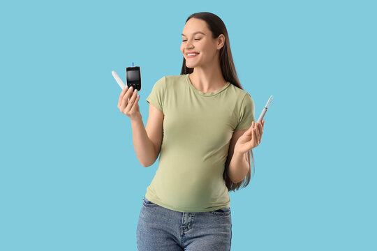 Young pregnant woman with gestational diabetes holding glucometer and lancet pens on blue background