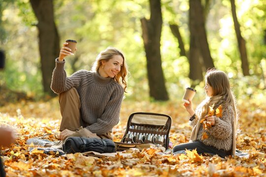 Fashionable young mother with a little daughter have a picnic in autumn park