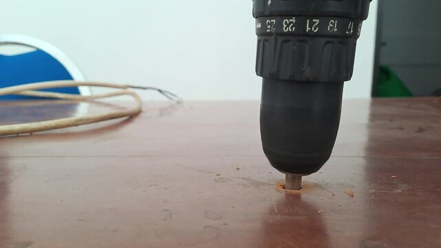 Technician drilling wooden library table with power drill for electrical outlet installation. Worker assembling socket wiring. Construction stock video 4K for DIY, renovation, carpentry, maintenance, 