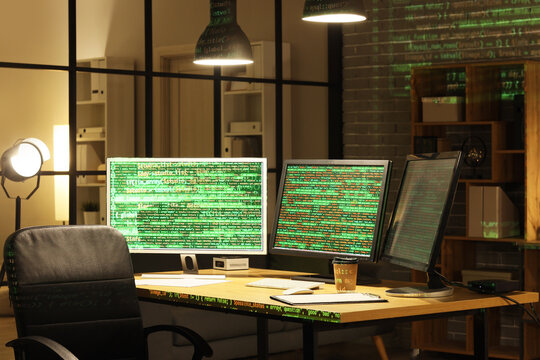 Computer monitors with programming code on table in dark office at night