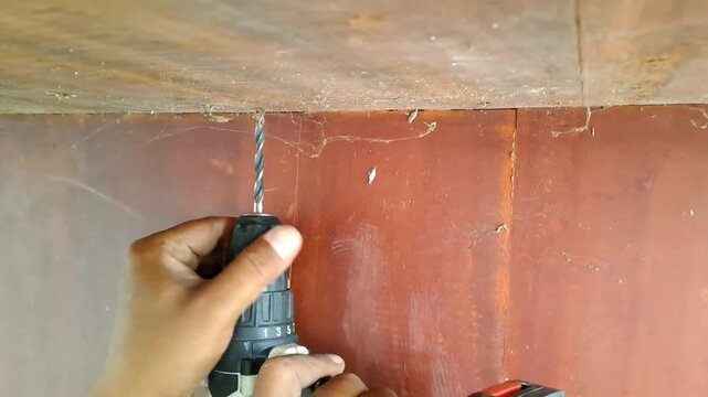 Technician drilling wooden library table with power drill for electrical outlet installation. Worker assembling socket wiring. Construction stock video 4K for DIY, renovation, carpentry, maintenance, 