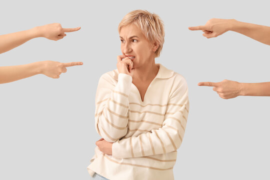 People pointing at worried mature woman on light background. Accusation concept