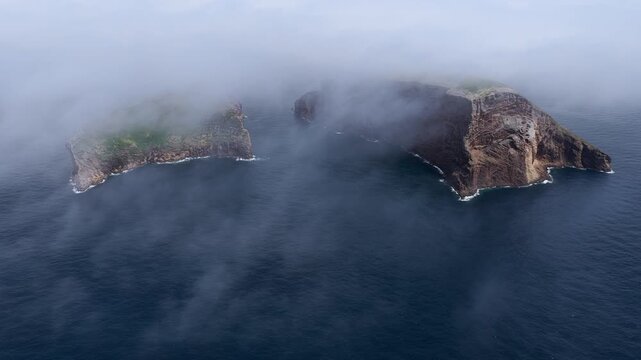 Aerial view of Ilheus das Cabras surrounded by mist and ocean waves in the Azores, Portugal.