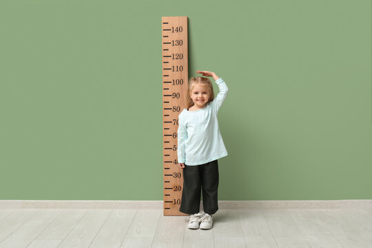Cute little girl measuring height near green wall