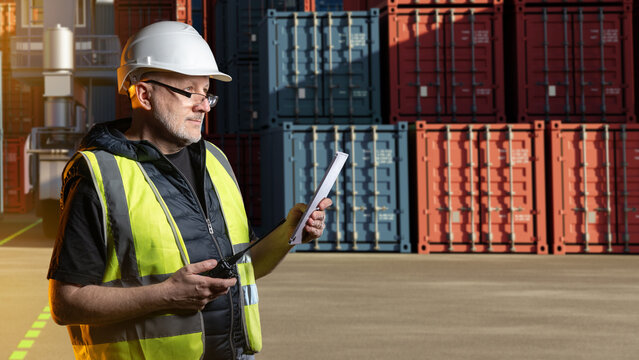 Container terminal, logistics supervisor checks cargo documents and radio communication near shipping containers at industrial freight yard