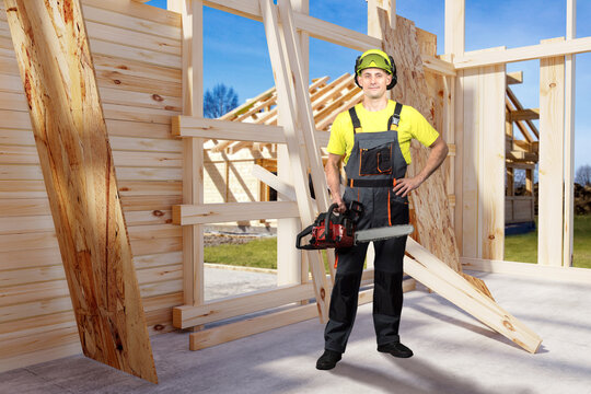 Construction framing carpenter cuts timber beams using chainsaw at residential wooden house structure under building development site