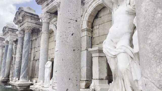 Close pan shot of intricately carved marble statues and structural pillars inside the Antonine Nymphaeum fountain house in Sagalassos, Turkey.