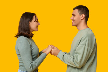Fototapeta premium Happy young couple holding hands and smiling at each other on yellow background