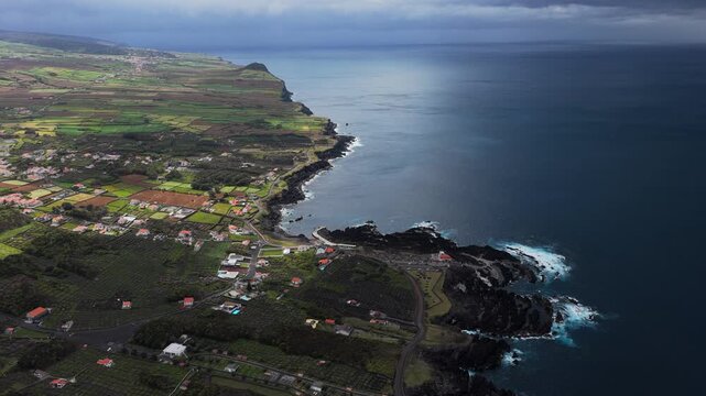 Aerial view of the volcanic rock pools and lush green fields along the rugged coastline of Biscoitos, Azores, Portugal.